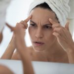 Woman creasing and stretching her forehead while looking in the bathroom mirror