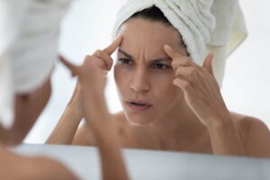 Woman creasing and stretching her forehead while looking in the bathroom mirror